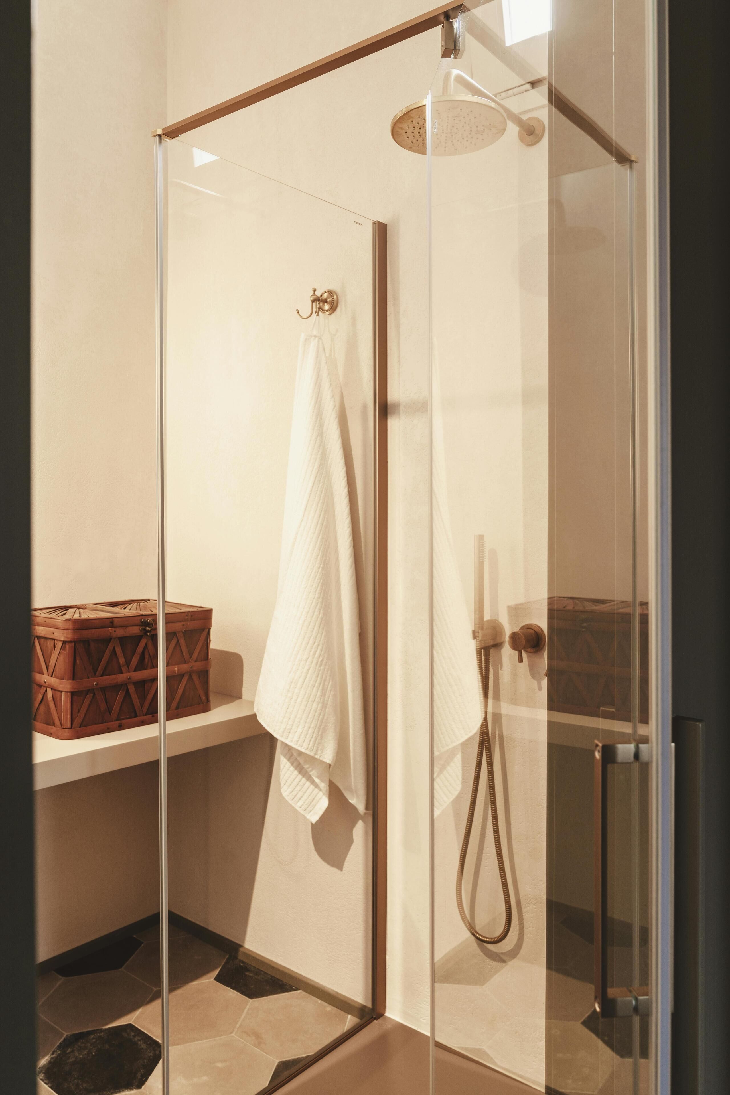 A glass-enclosed shower with a handheld showerhead, a towel hanging on the wall, and a wooden box on a shelf.