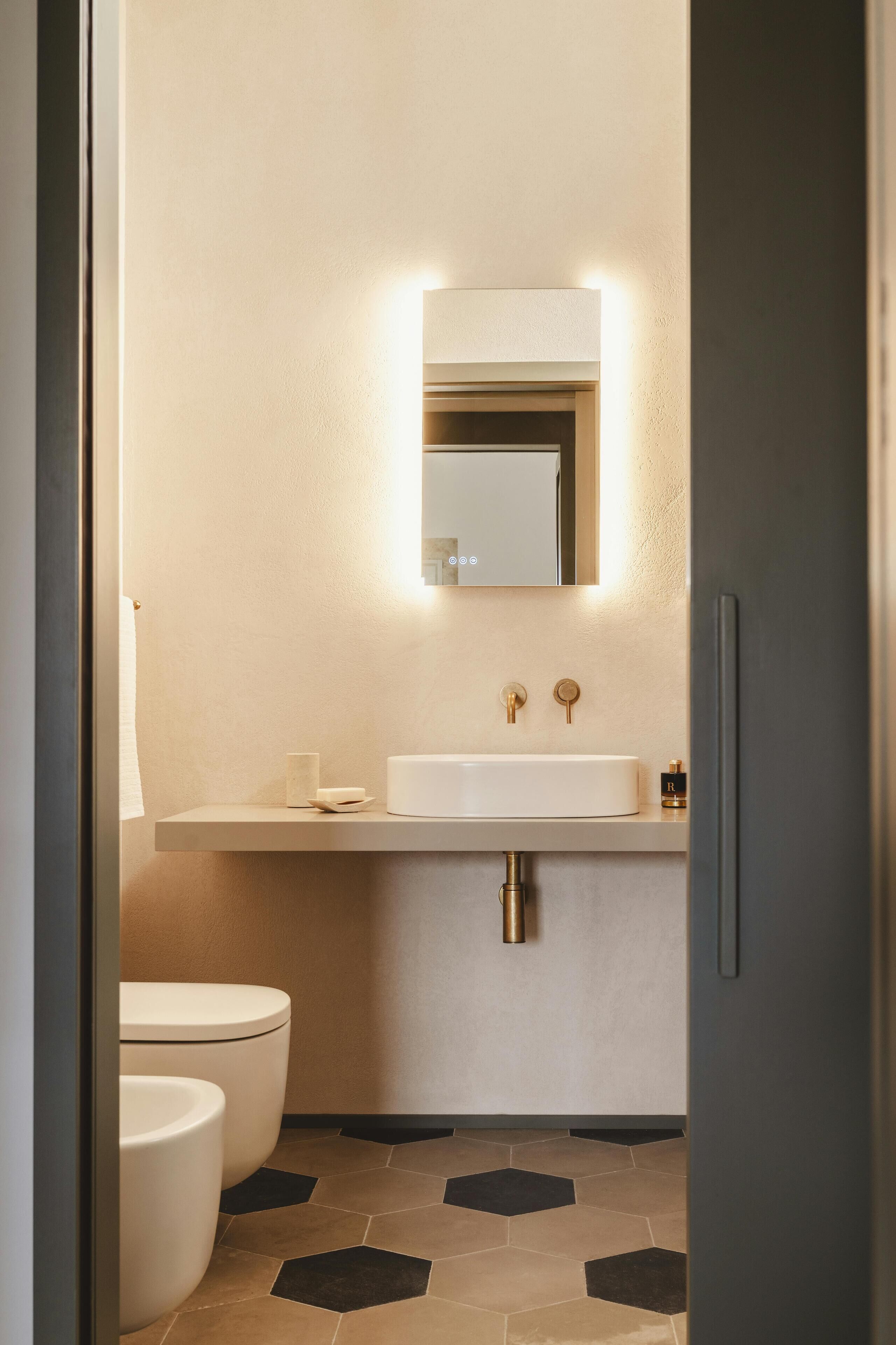 A modern bathroom with a white sink, a mirror, and two toilets.