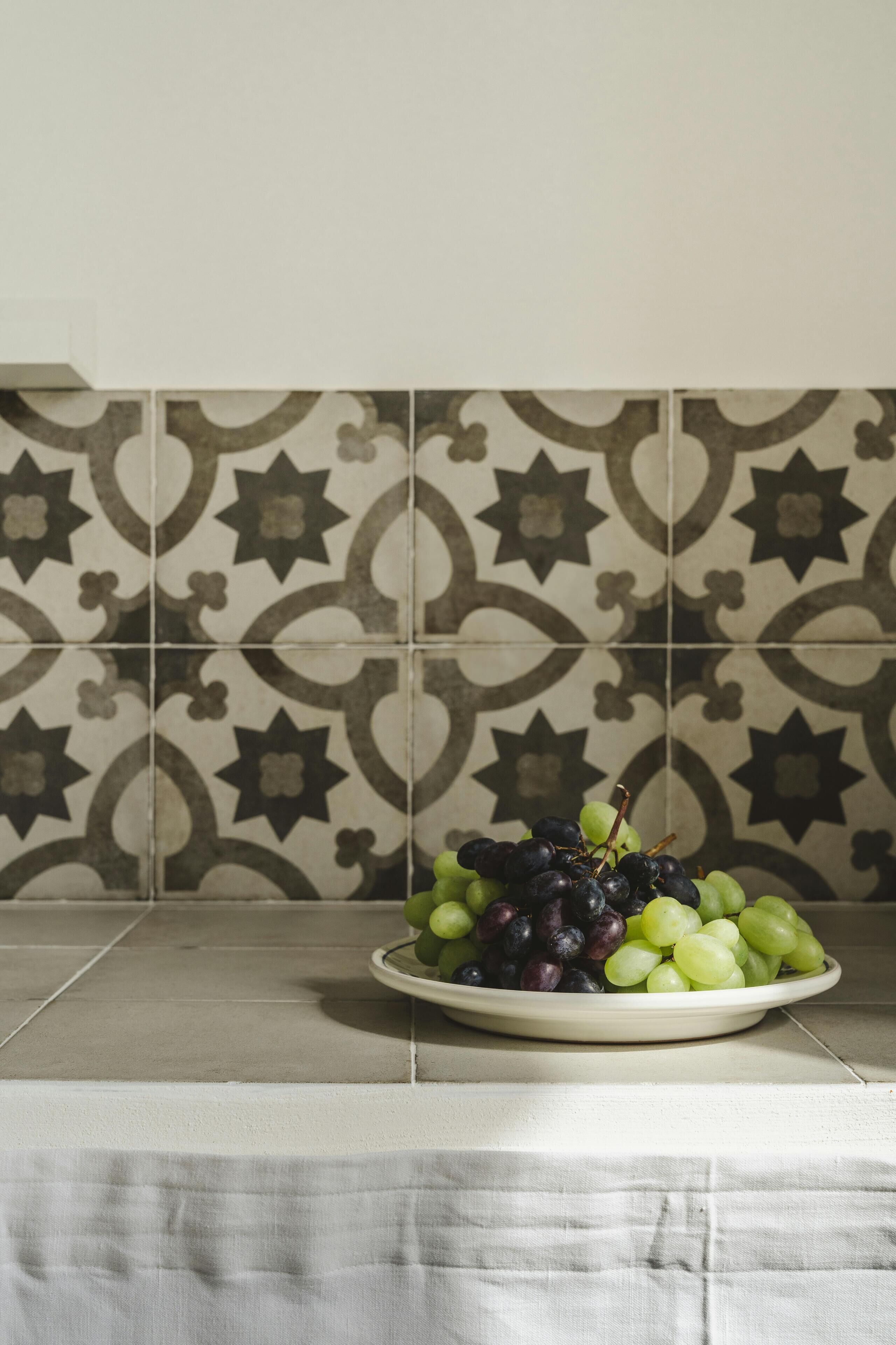 A plate of mixed grapes on a table with a patterned tile backsplash.
