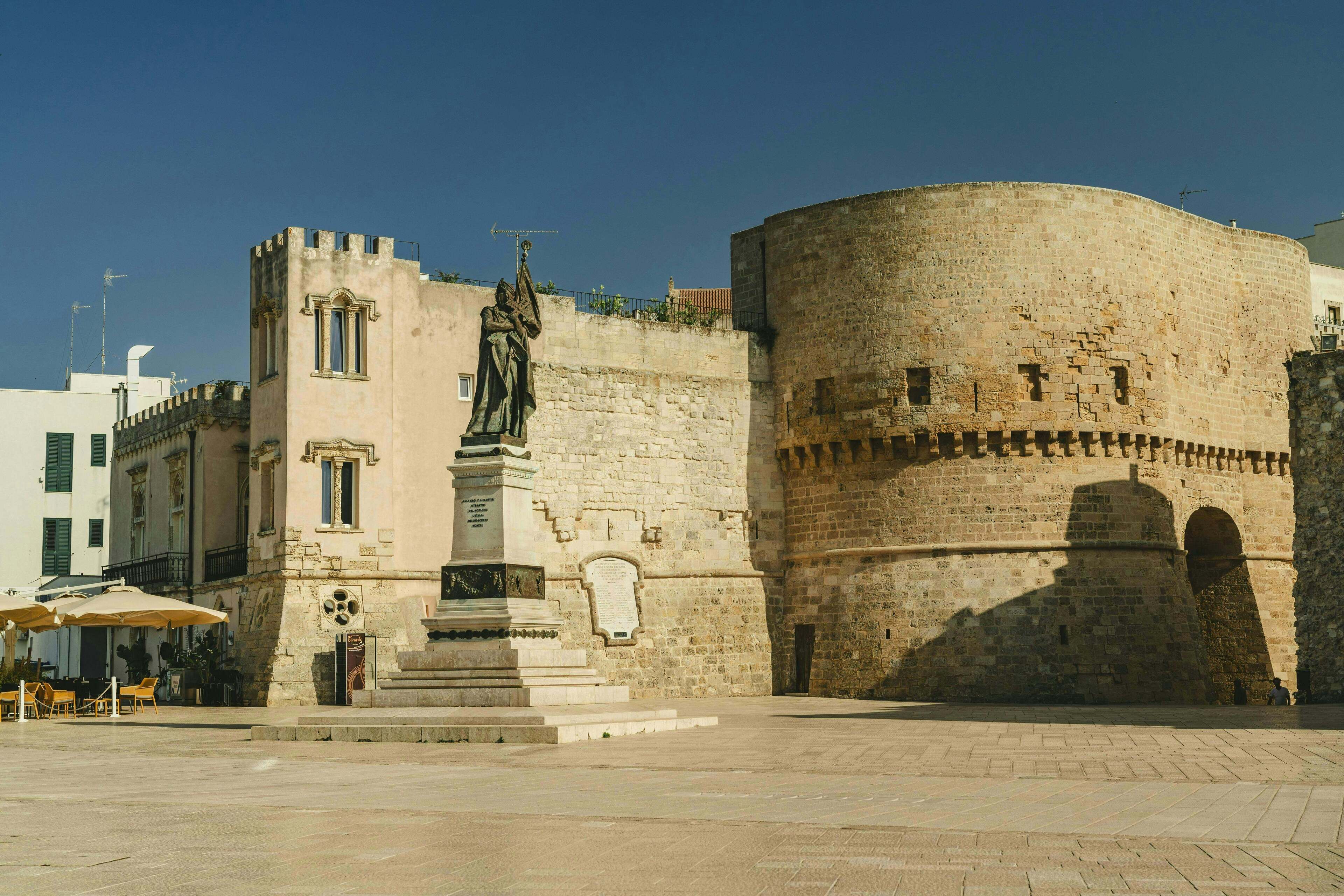 Un bâtiment historique en pierre, avec une statue à l’avant, une cour et une tour ronde.