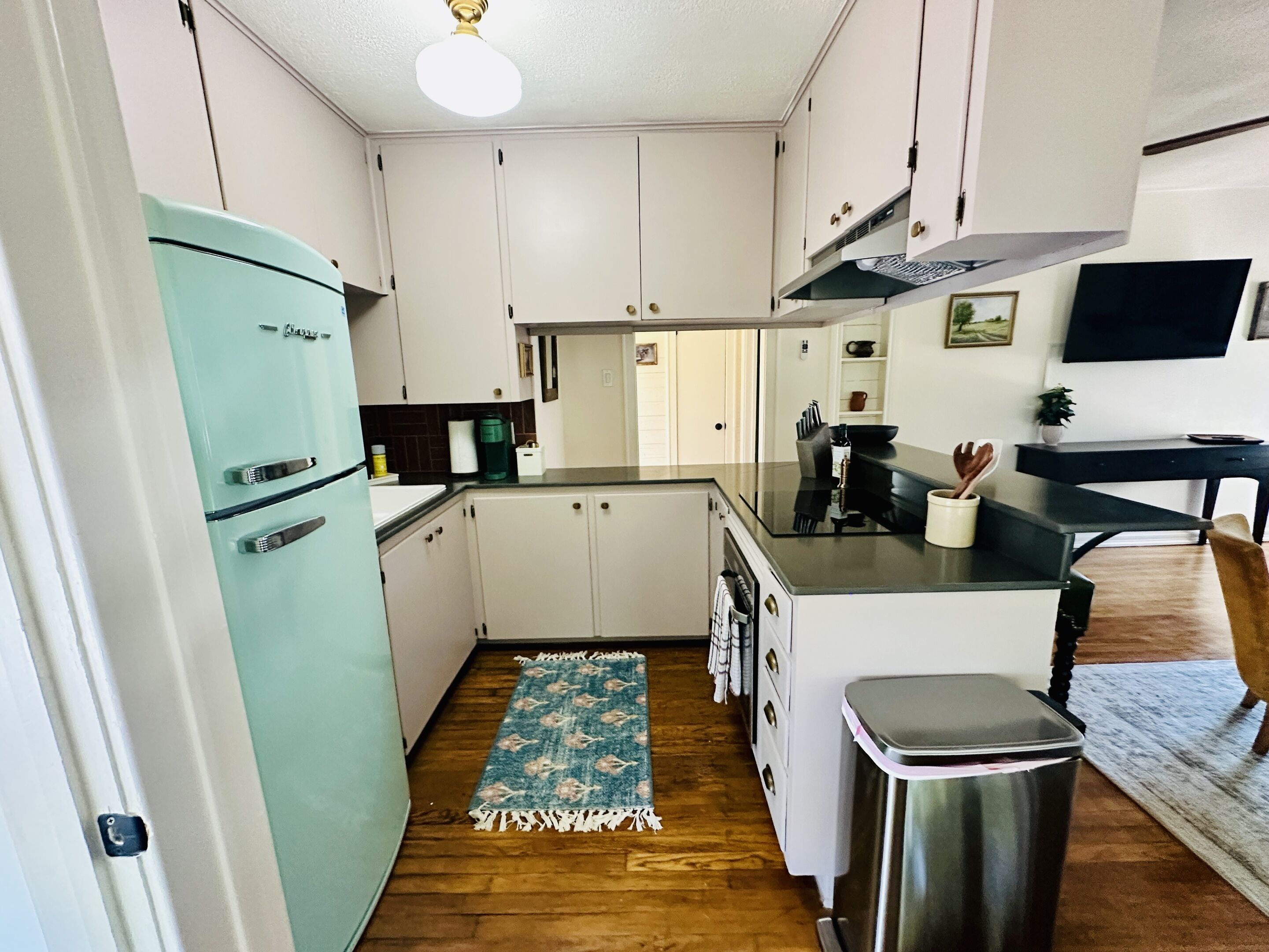 Une cuisine compacte avec des meubles blancs, un réfrigérateur turquoise et un petit îlot central doté d’un évier.