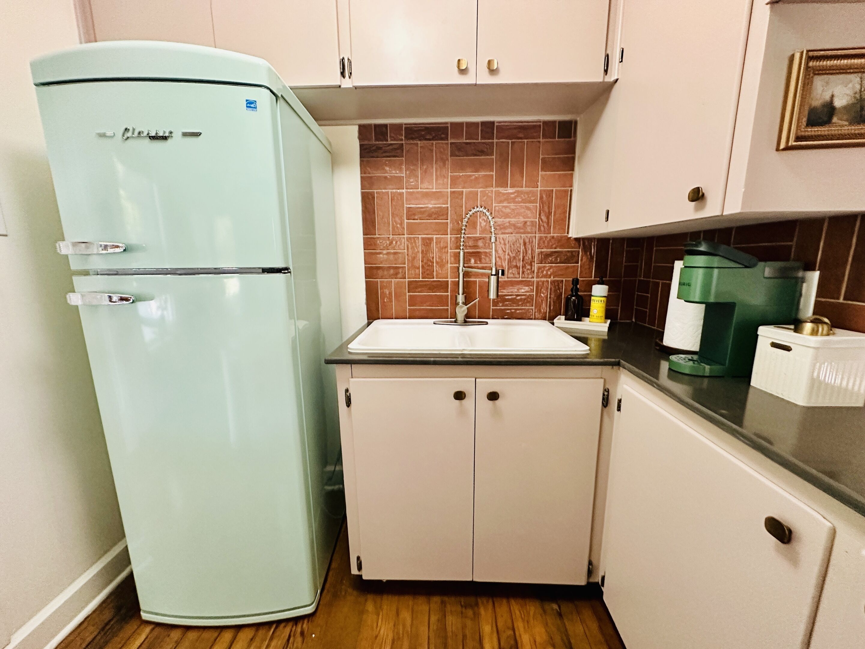 Una cocina compacta con un refrigerador de estilo vintage, un lavamanos y una cafetera.