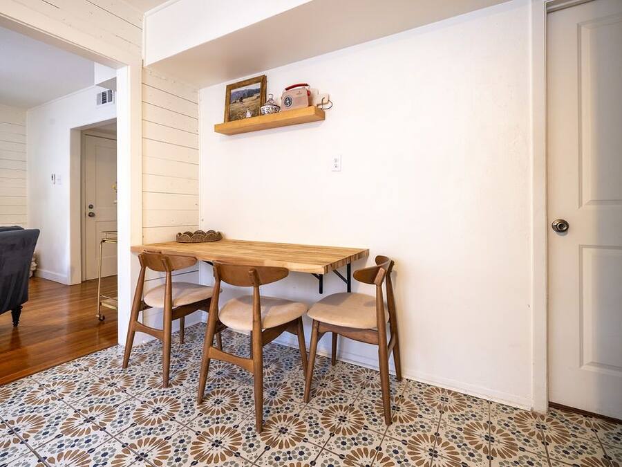 Un comedor con una mesa de madera y cuatro sillas, una estantería con adornos, y un suelo con diseño.