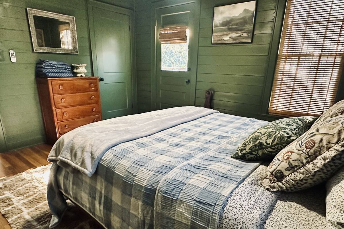 A bedroom with a bed, dresser, and a window with blinds.