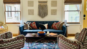 Een gezellige woonkamer met een blauwe bank, gestreept fauteuils, een salontafel en een kleurrijk vloerkleed.