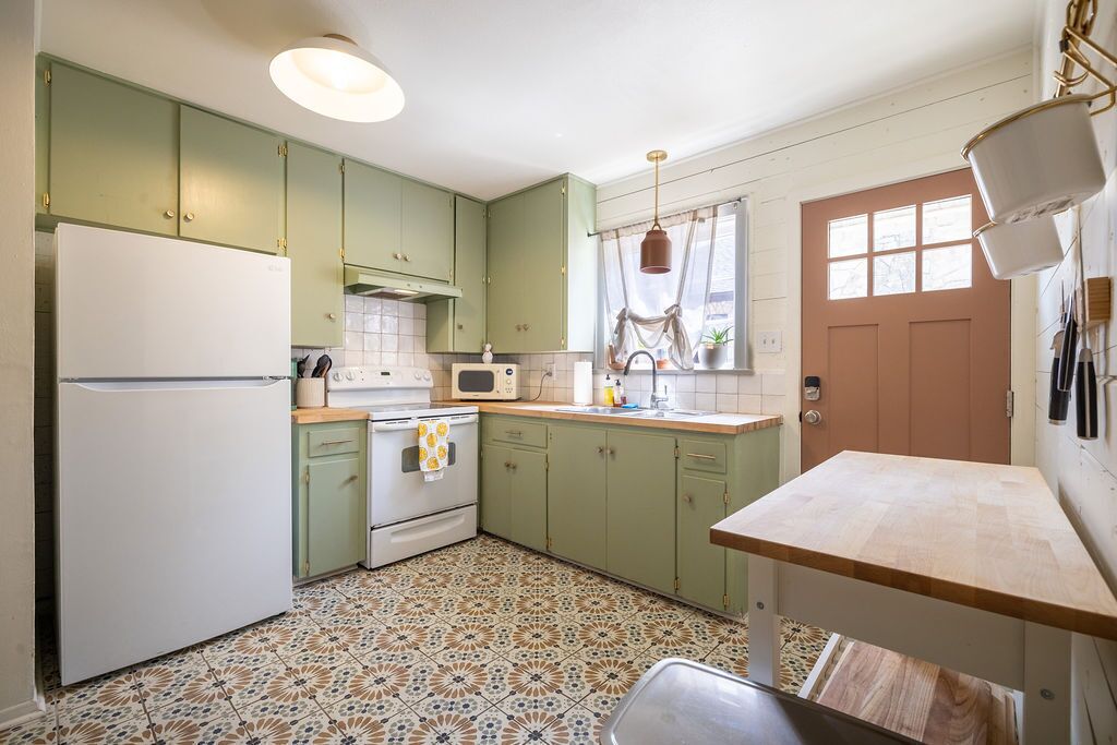 A kitchen with green cabinets, a white refrigerator, a microwave, and a wooden countertop.