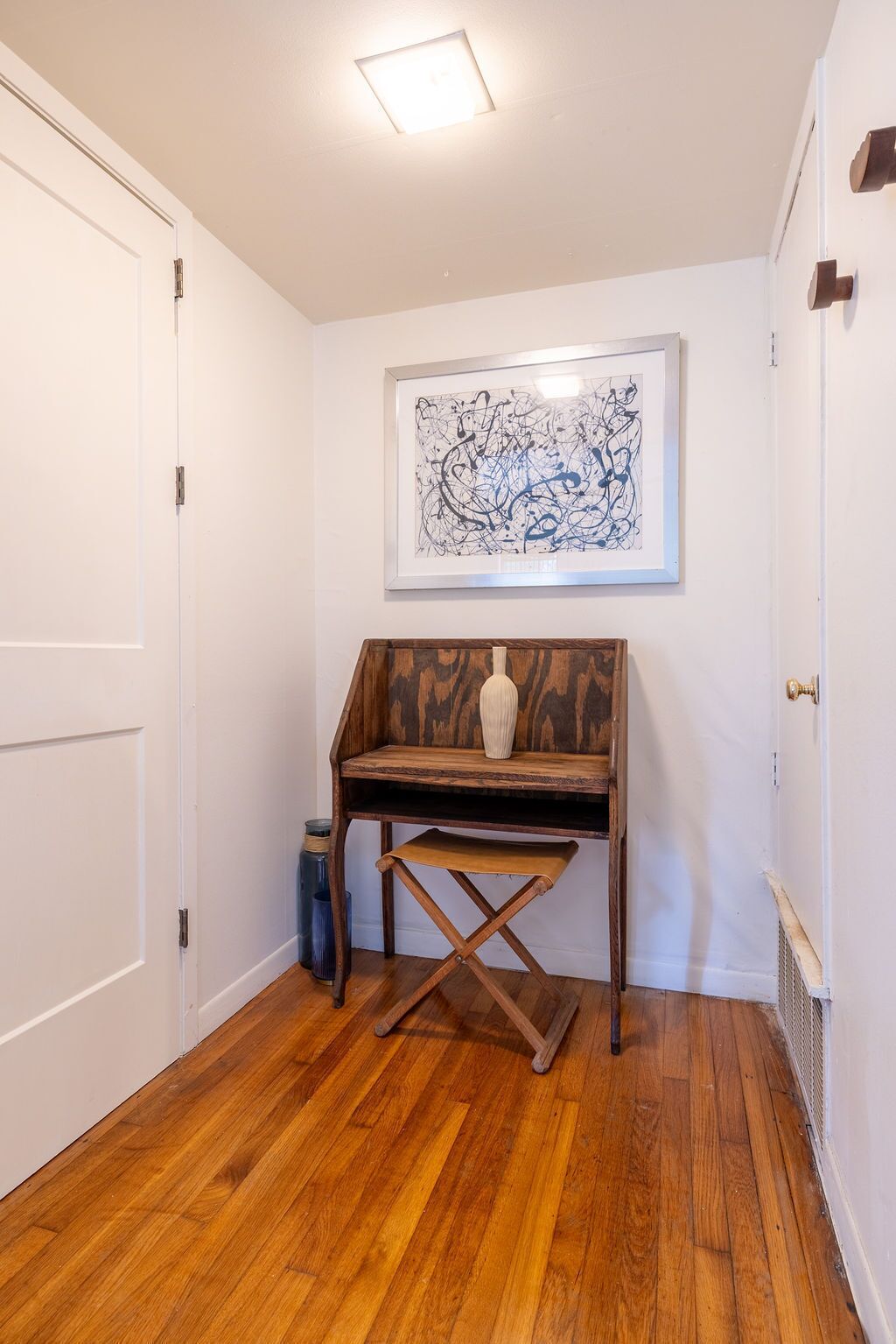 A hallway with a wooden desk, a framed abstract painting, and a white door.