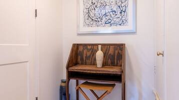 A hallway with a wooden desk, a framed abstract painting, and a white door.