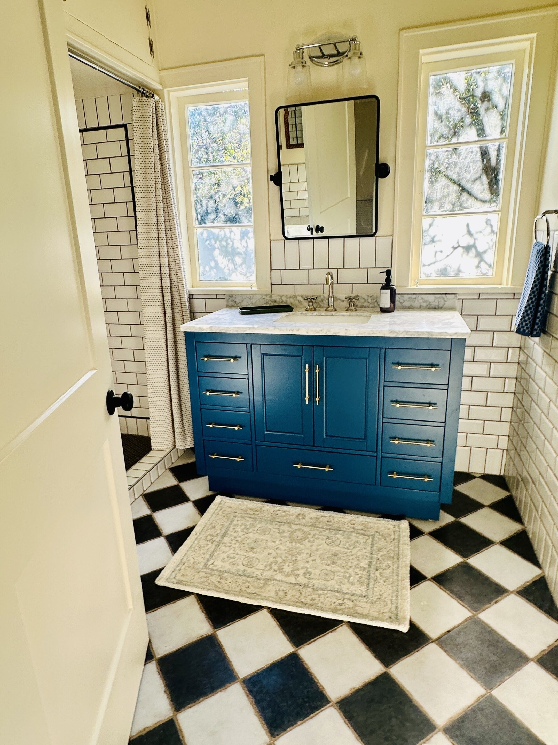 A bathroom with a blue vanity, a mirror, a sink, and a patterned rug.
