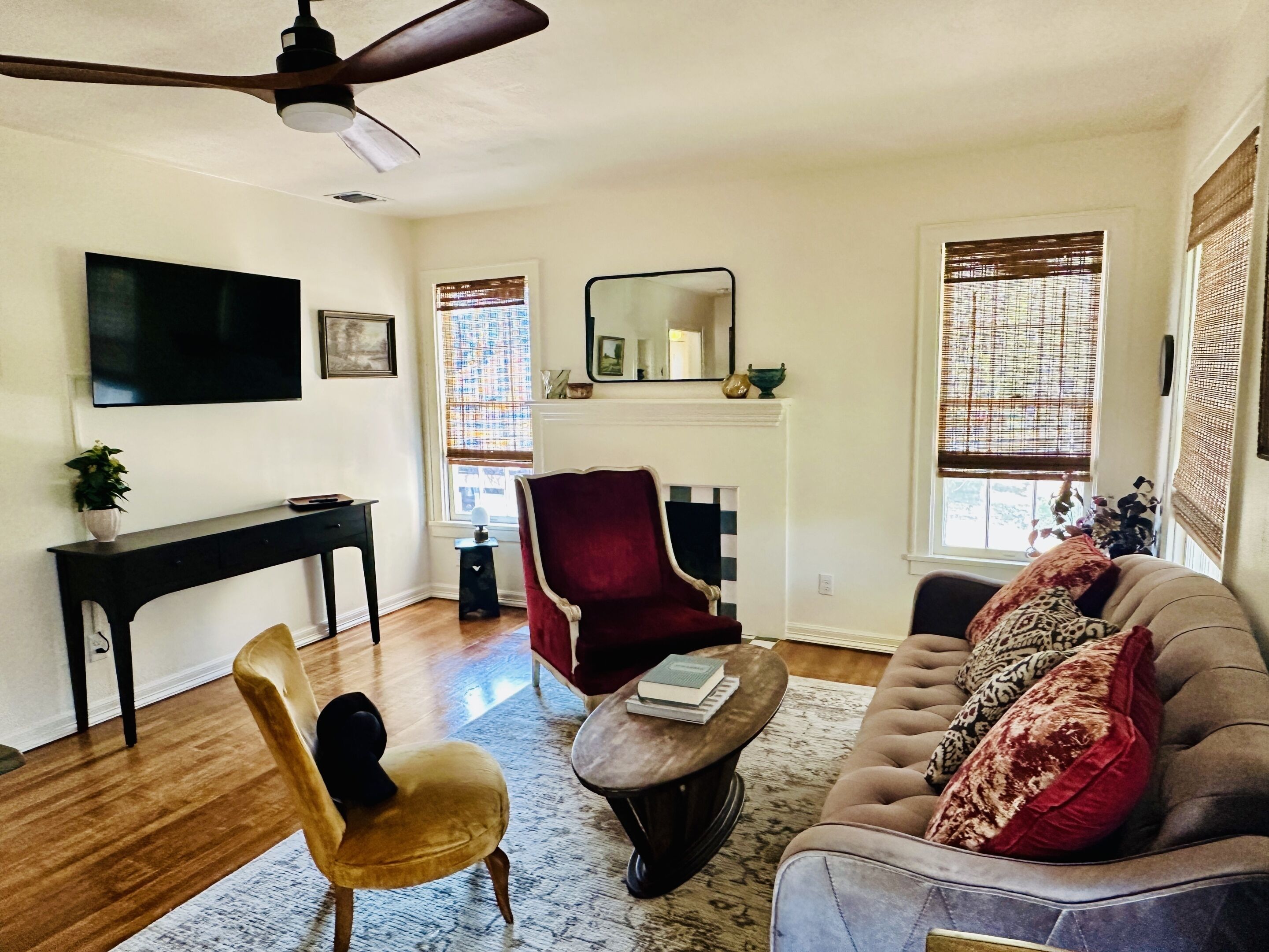 Una sala de estar con televisión, chimenea, un sillón rojo, sofá y ventilador de techo.