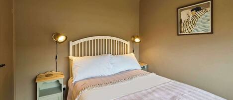 A bedroom with a white bed, two bedside lamps, a nightstand, and a wall-mounted painting.
