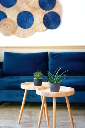 A room with a blue sofa, two round wooden tables with potted plants, and a wall art piece. - Charming 3-bedroom villa with heated pool and AC in Fronsac accross a river (Fronsac)