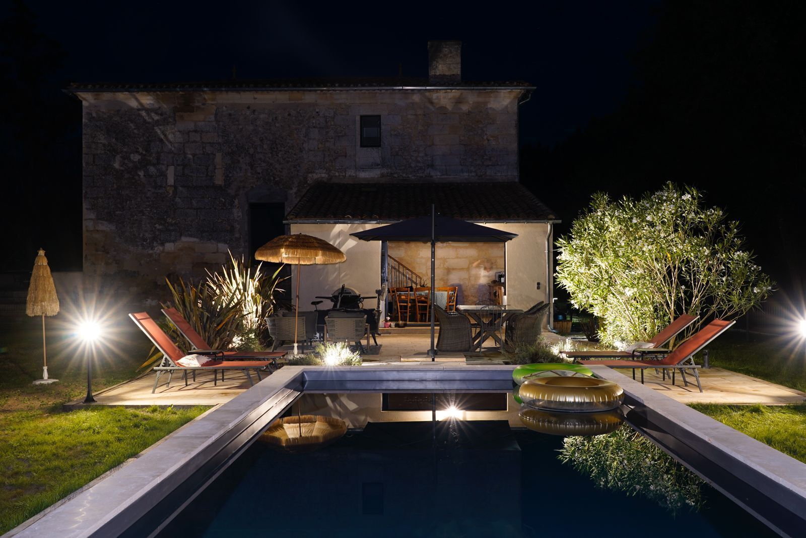 A stone house with a swimming pool, outdoor furniture, and a well-lit patio area.