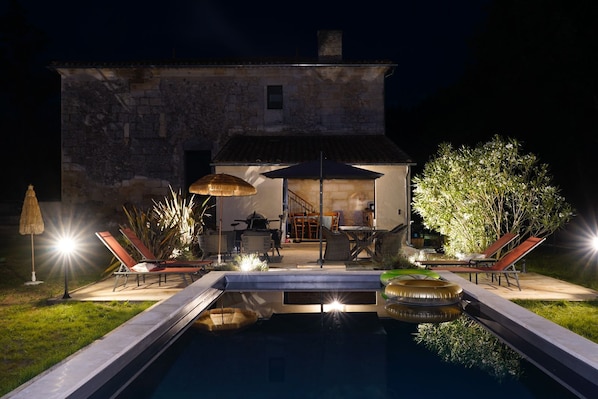 Una casa de piedra con piscina, mobiliario de exterior y un patio bien iluminado.
