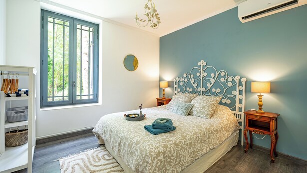 A bedroom with a bed, two bedside tables, a chandelier, and a window with blinds. - Charming 3-bedroom villa with heated pool and AC in Fronsac accross a river (Fronsac)