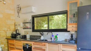 A kitchen with a dining table, chairs, a refrigerator, and a window with a view of greenery.