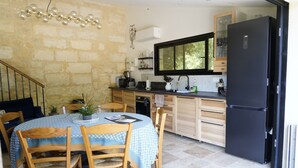 A compact kitchen with a dining area, featuring a black refrigerator, wooden cabinets, and a dining table set with chairs. - Charming 3-bedroom villa with heated pool and AC in Fronsac accross a river (Fronsac)