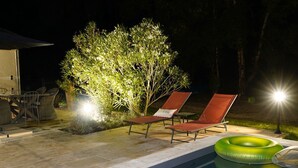 A poolside area with two lounge chairs, a table with chairs, and a small table with a lamp.