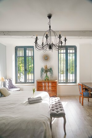 Un dormitorio con cama, banca, cómoda, silla y candelabro.