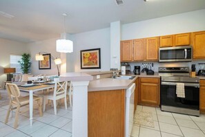 A modern kitchen with wooden cabinets, stainless steel appliances, and a dining area with white chairs and a table.