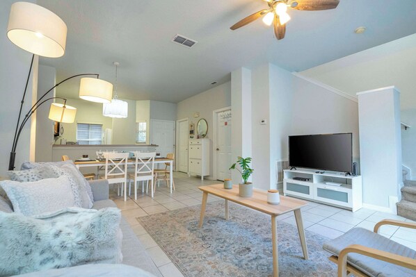 A modern living room with a sofa, a coffee table, and a TV. There is a dining area with a table and chairs.