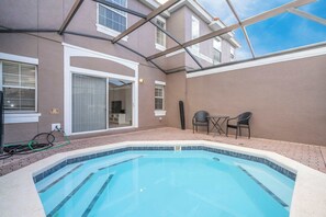 Une piscine dotée d’un toit en verre, un espace patio avec des chaises et une porte-fenêtre coulissante donnant sur une pièce.