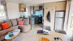 A modern living space with a sofa, a dining table, and a kitchen area. - ZEcamping 4 étoiles familial 1km plage espace aquatique mobil-home 36m2 (Les Mathes)