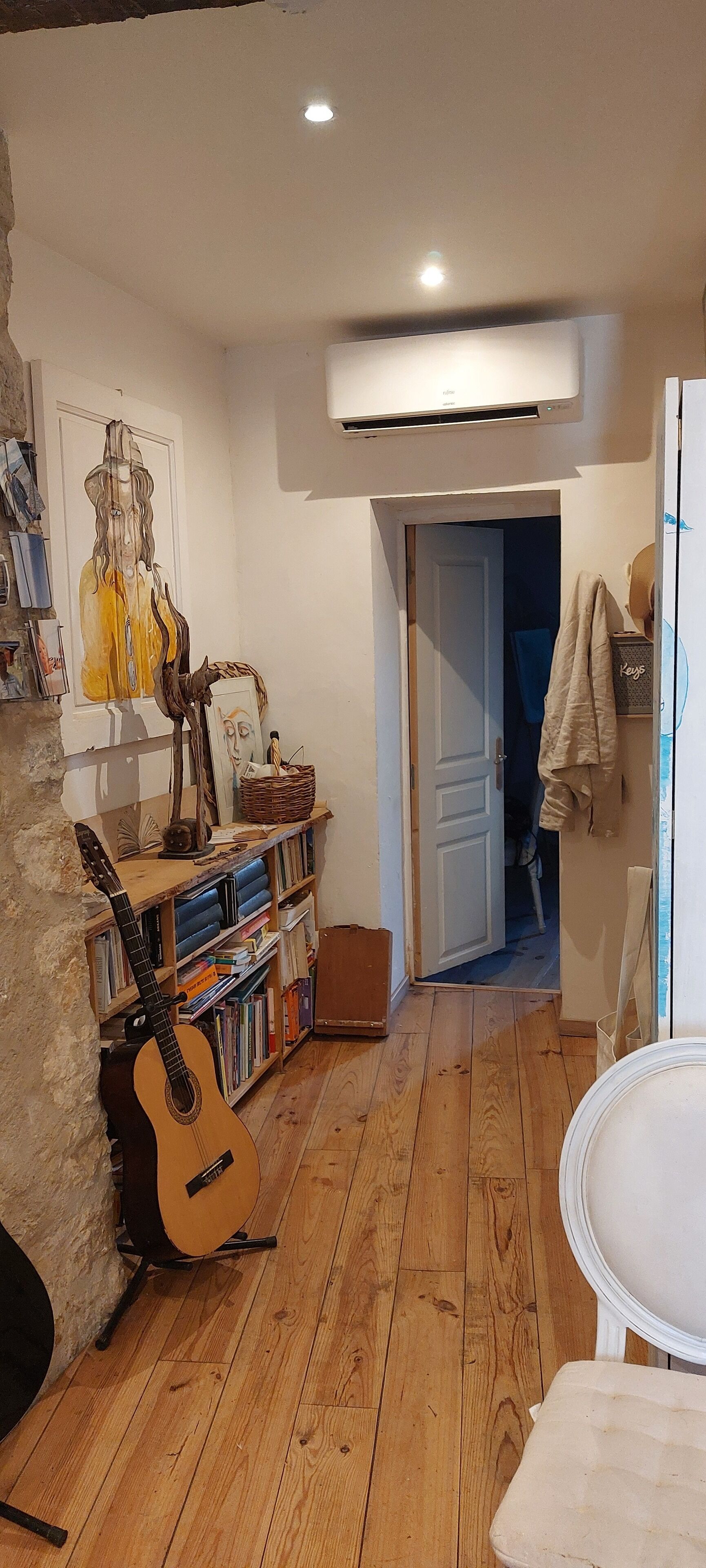 A room with a wooden floor, a guitar, a bookshelf, and a door leading to another room.