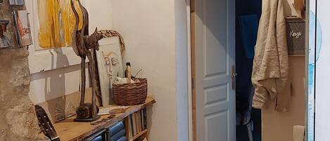 A room with a wooden floor, a guitar, a bookshelf, and a door leading to another room.