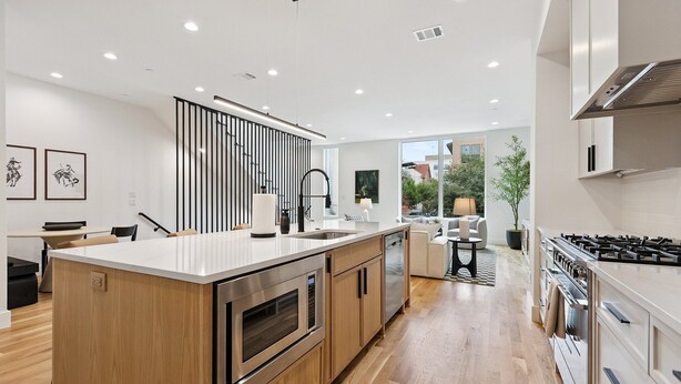 A modern kitchen with a large island, stainless steel appliances, wooden cabinets, and a view of the outdoors. - The Eastwood Escape (Dallas)