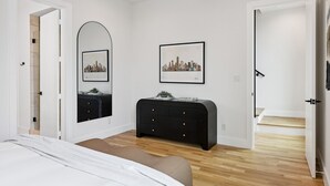 A bedroom with a bed, a dresser, a mirror, and a framed cityscape picture on the wall. - The Eastwood Escape (Dallas)