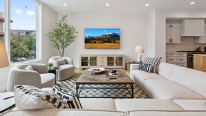 A modern living room with a large window, a sofa, a coffee table, and a cabinet. - The Eastwood Escape (Dallas)