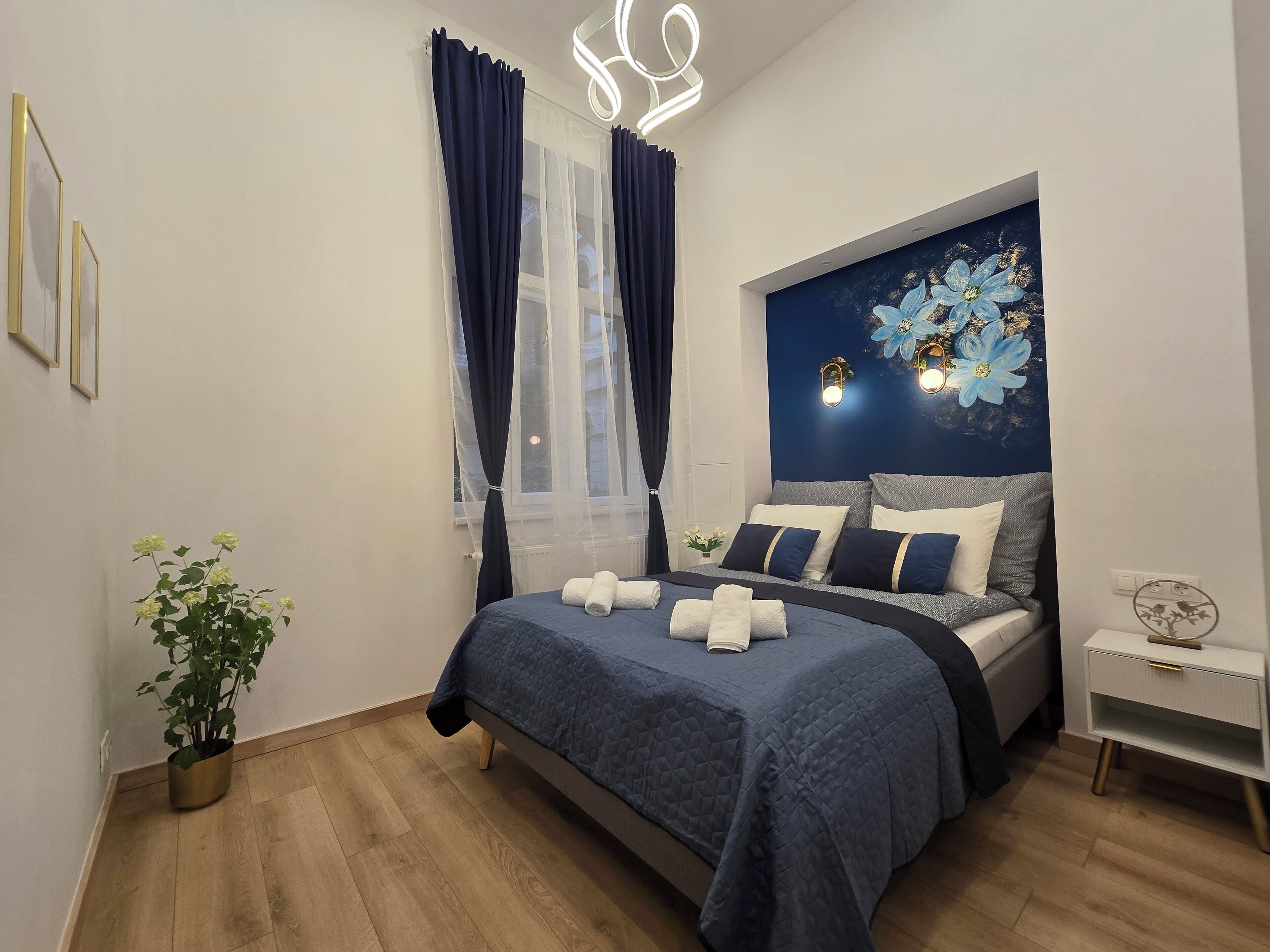 A modern bedroom with a bed, bedside tables, a potted plant, and a decorative wall piece.