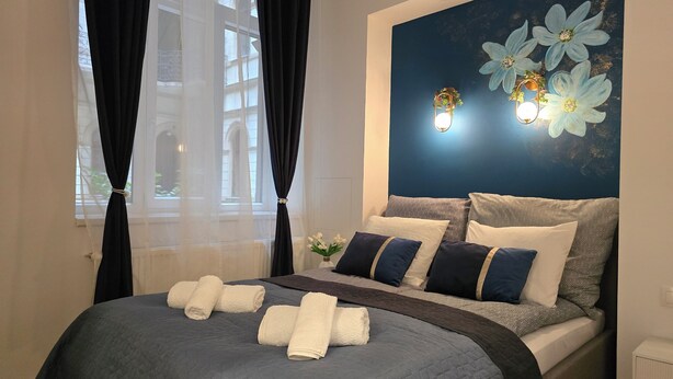 Une chambre d’hôtel avec un lit, un mur décoré de motifs floraux et une fenêtre ornée de rideaux légers.
