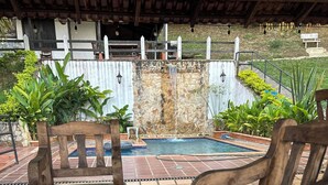 Um banco de madeira e um laptop numa varanda pavimentada, com uma piscina ao fundo.