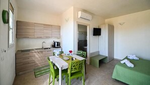 Una cucina compatta con zona pranzo, un tavolino e un letto singolo con copripiumino verde.