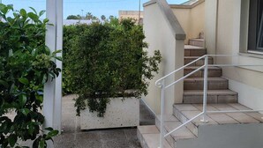 Un'area esterna coperta con una scala che conduce all'ingresso di un edificio, immersa nel verde e sotto un cielo sereno.