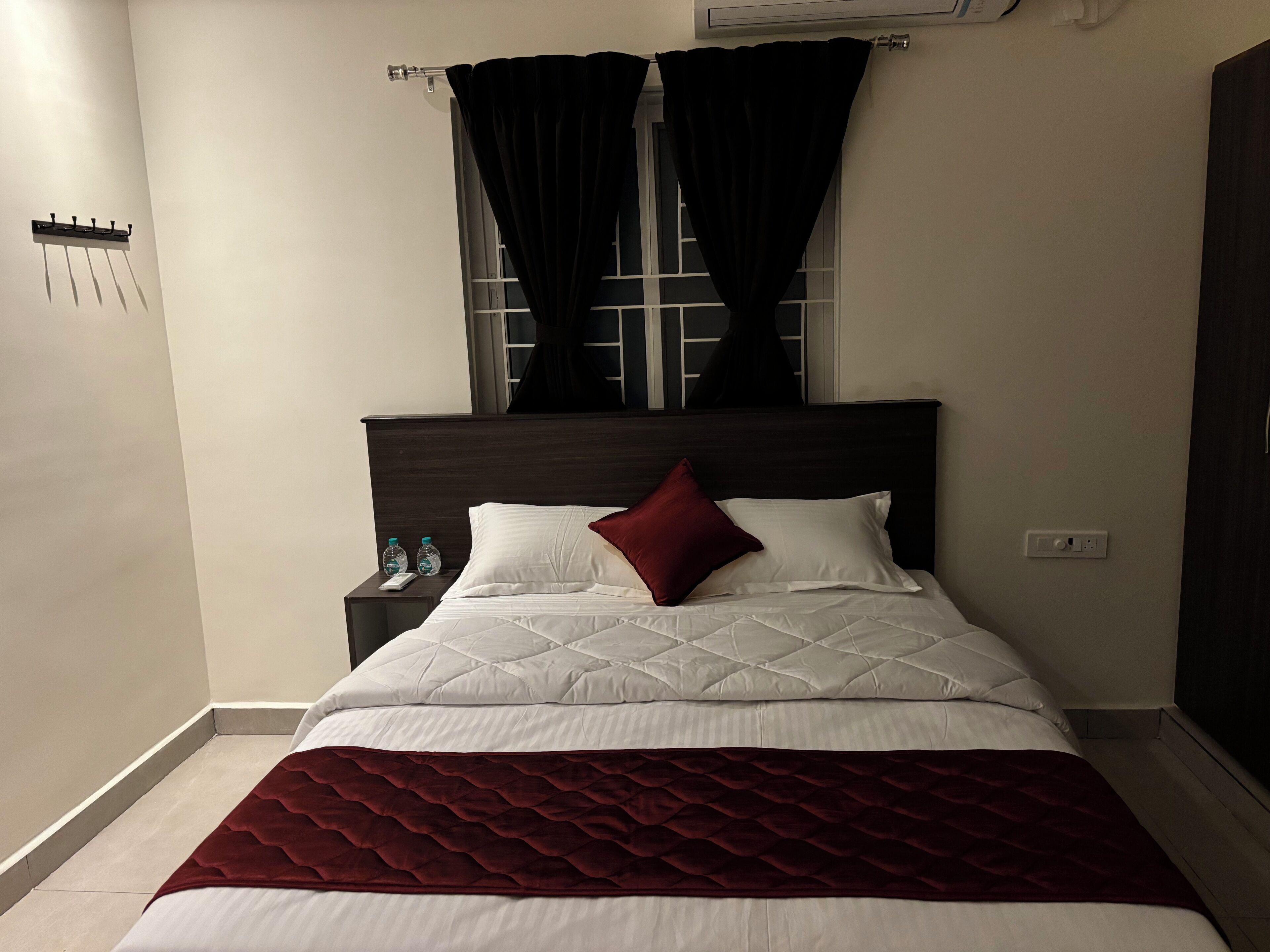 A neatly made bed with a quilted headboard, a dark red throw blanket, and two pillows.