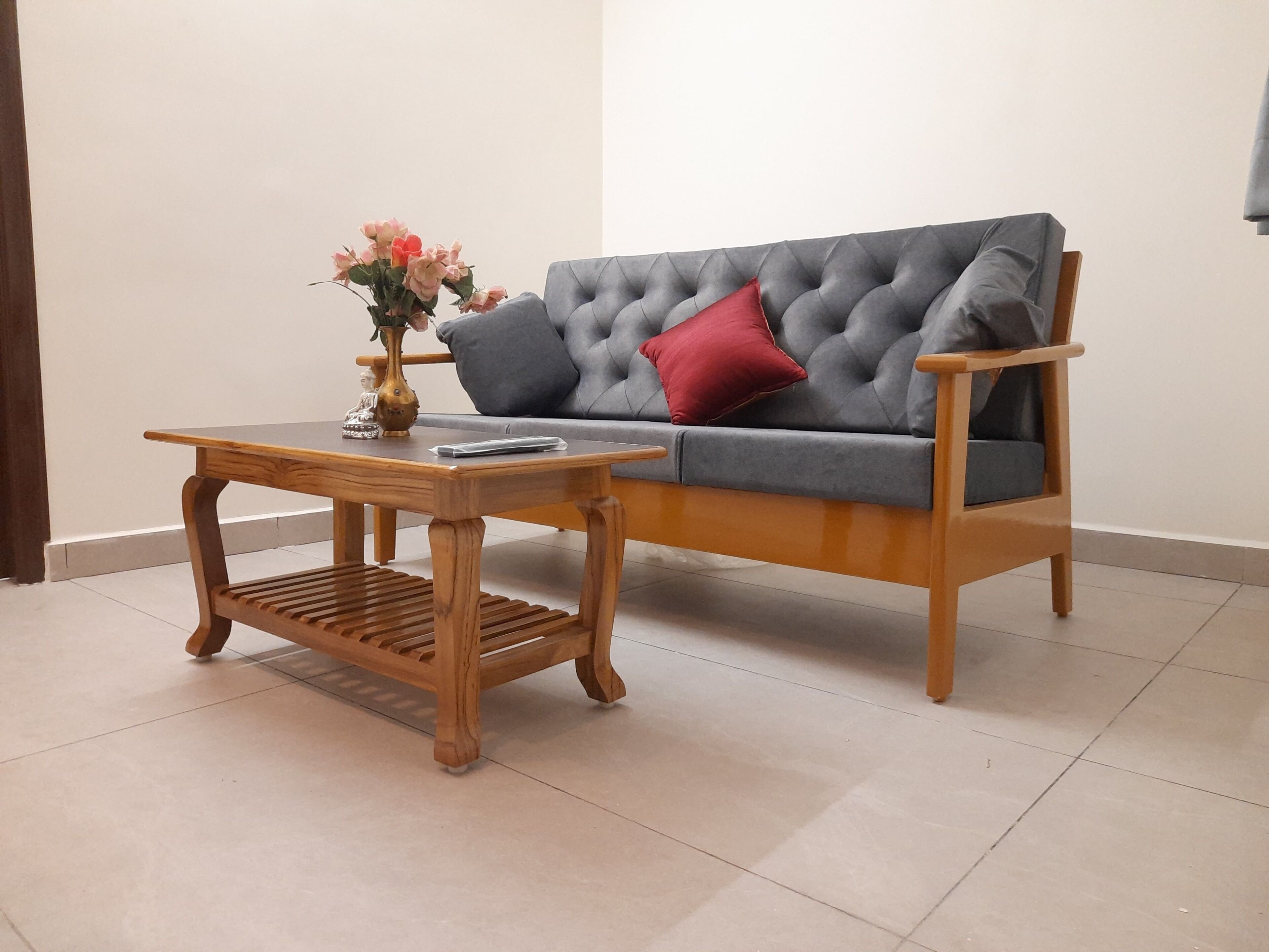 Un sofá gris con un cojín rojo, una mesa de centro de madera y un jarrón con flores.