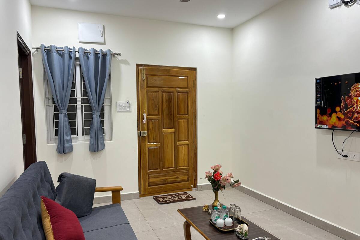 A living room with a sofa, a wooden door, a television, and a small table with decorative items.
