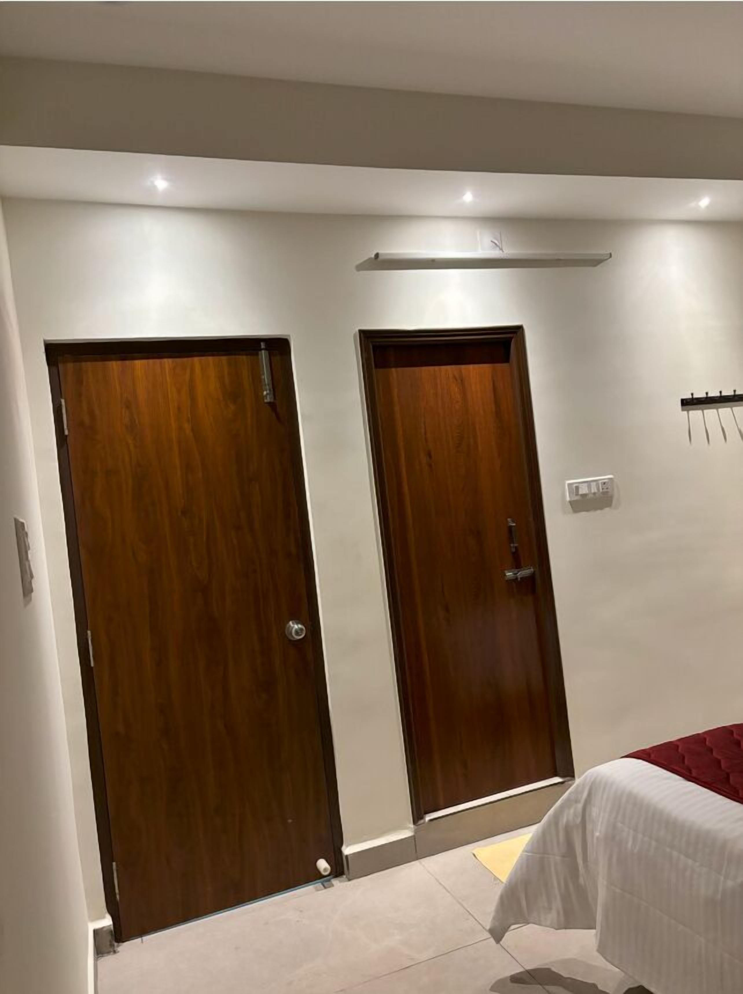 A bedroom with two wooden doors, a bed with a white bedspread, and a red blanket.