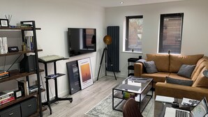 Un salon moderne avec un canapé, une table basse et un téléviseur. On y trouve également des étagères, une lampe sur pied et un radiateur.