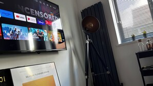 Un salon moderne doté d’un grand téléviseur à écran plat diffusant divers services de streaming, d’un lampadaire, d’une affiche du film « Blade Runner 2049 » et d’un radiateur.