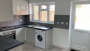 Une cuisine compacte équipée d’une cuisinière à gaz, d’un four, d’un lave-linge et d’une fenêtre donnant sur un jardin.