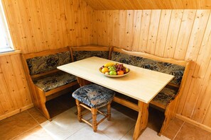 Ein Zimmer mit Holzboden, einer Bank und einem Tisch, auf dem eine Obstschale steht, und mit gemusterten Kissen.