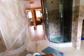Eine gläserne Dusche mit gefliestem Boden, eine hölzerne Sitzbank und eine Glastür zu einem Raum mit einem Bett und einem Fenster.