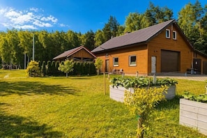 A two-story wooden house with a garage, surrounded by a well-maintained lawn and trees.