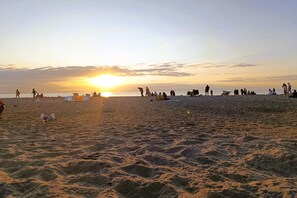 Ein Strand mit Menschen und Vögeln bei Sonnenuntergang.