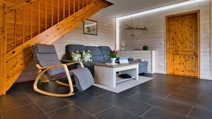 Una sala de estar moderna con una escalera de madera, un conjunto de sofá gris, una mesa de centro blanca y una puerta de madera.