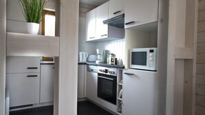 Una cocina compacta con armarios blancos, microondas, horno y cafetera.